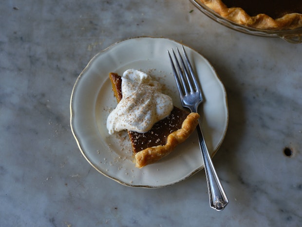 a spice of pumpkin pie on a plate with a golden crust and dollop of whipped cream