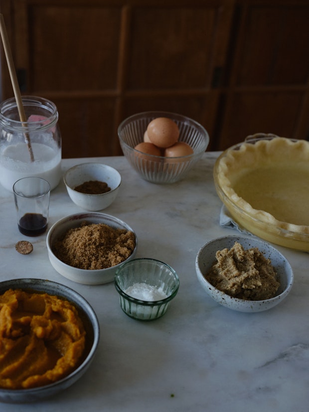 ingredients to make a pumpkin pie arranged on counter including eggs, brown sugar, pumpkin puree, and vanilla