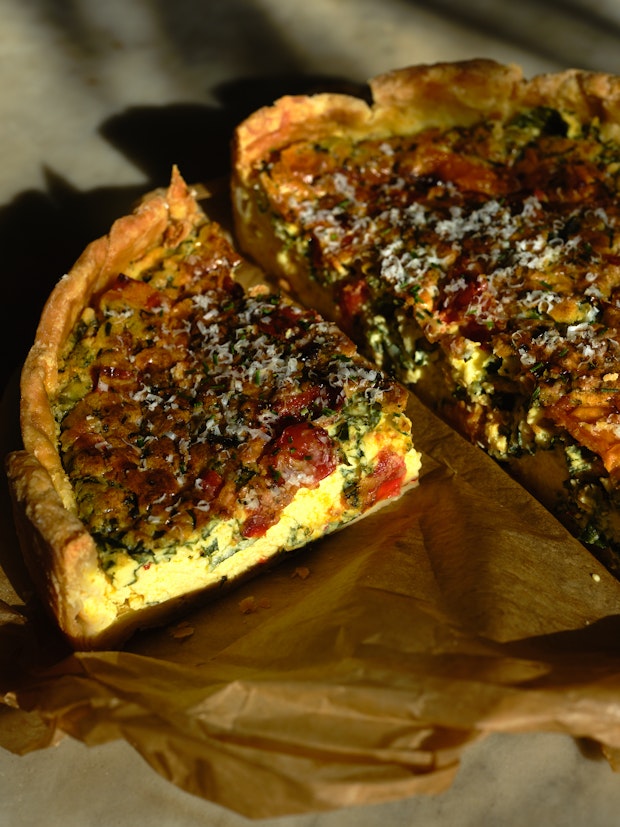 a wedge of quiche on a piece of parchment paper with a deep-dish golden crust