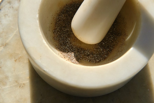 Cardamom pods being crushed in a white mortar and pestle