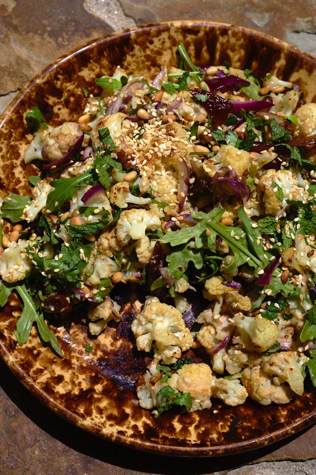roasted cauliflower on a platter with tahini glaze, mint, herbs, dates and more