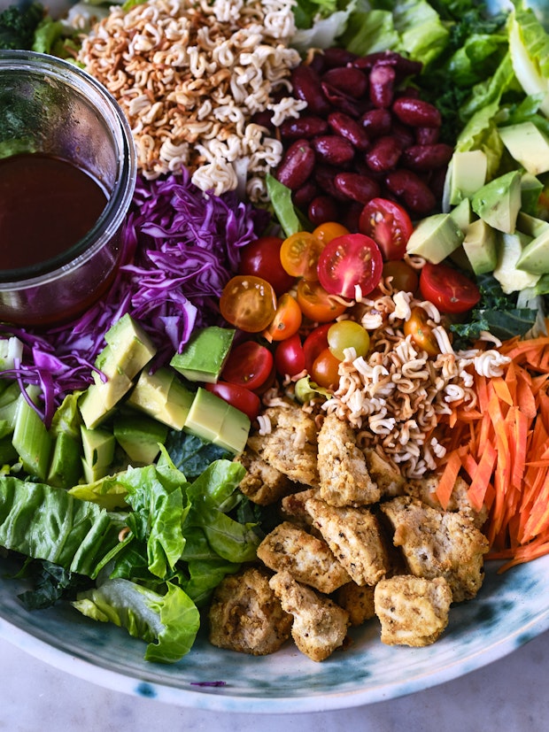 salt and pepper tofu in a large bowl with salad ingredients like ramen noodles, shredded lettuce and carrots