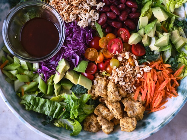 salt and pepper tofu in a large bowl with salad ingredients like ramen noodles, shredded lettuce and carrots