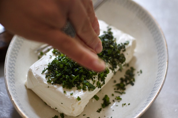 Sprinkling chives and herbs on a brick of cream cheese