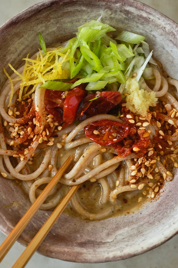 sesame noodles in a bowl with ginger, zest, and chile oil toppings