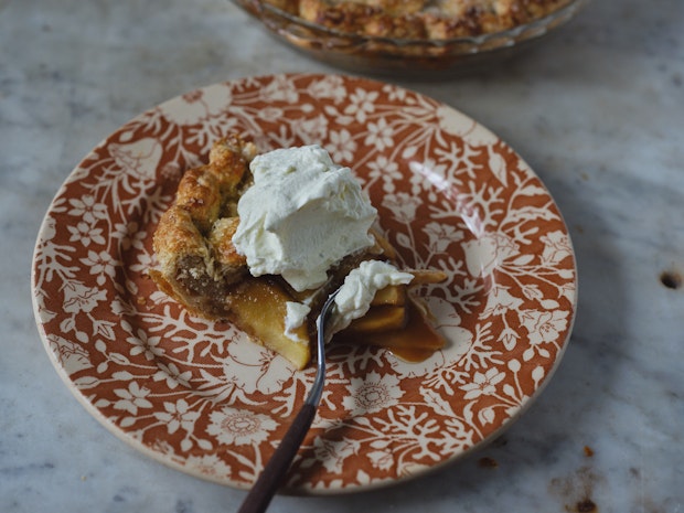 a slice of apple pie on a small plate topped with dollop of whipped cream