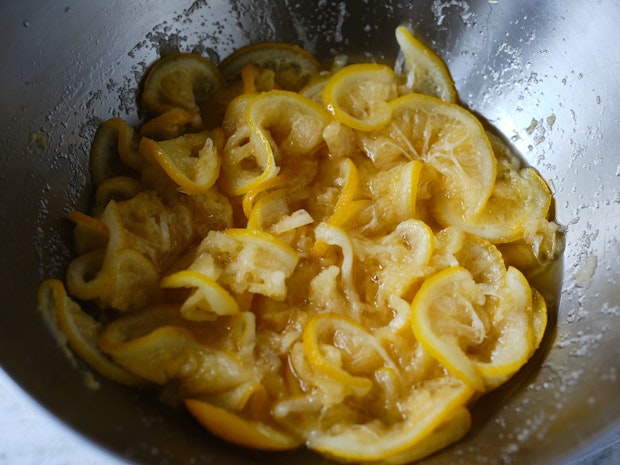 thinly sliced lemons macerating in a metal bowl with sugar