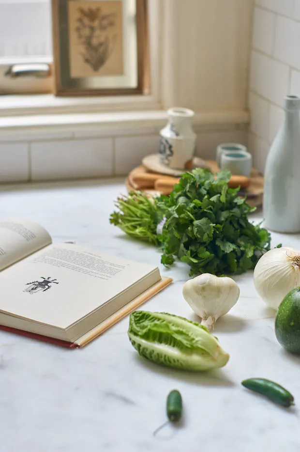 Ingredients for making Sopa Verde de Elote soup on a countertop including garlic, cilantro, onion