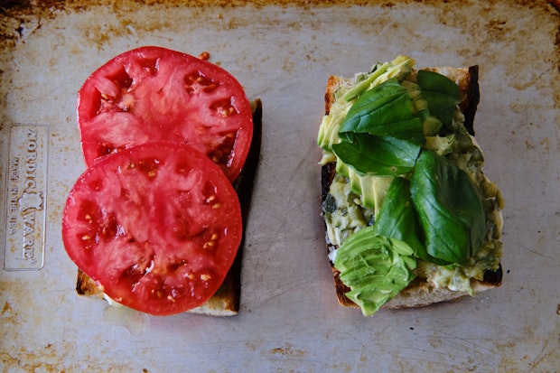 assembling a tomato sandwich by adding avocado and tomatoes