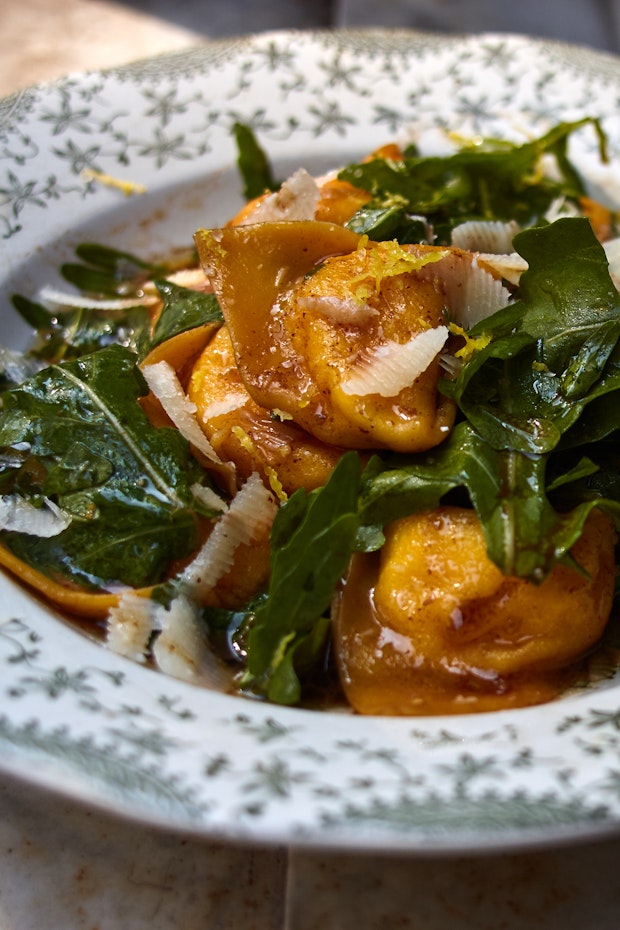 tortelli pasta in a bowl with brown butter sauce, arugula, and cheese