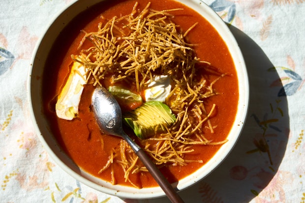tortilla soup in a bowl topped with tortilla strips, sliced avocado, and sour cream