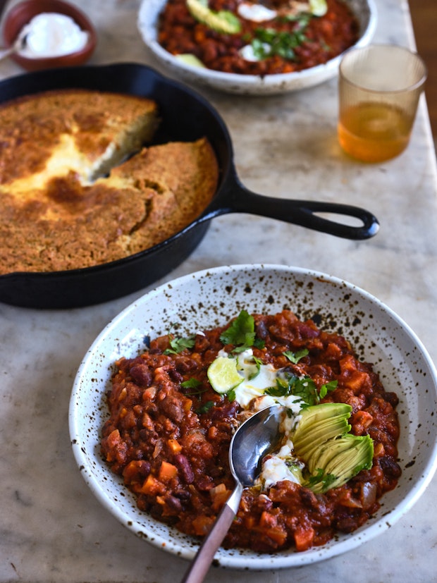 marble table topped with bowls of chili and a skillet cornbread