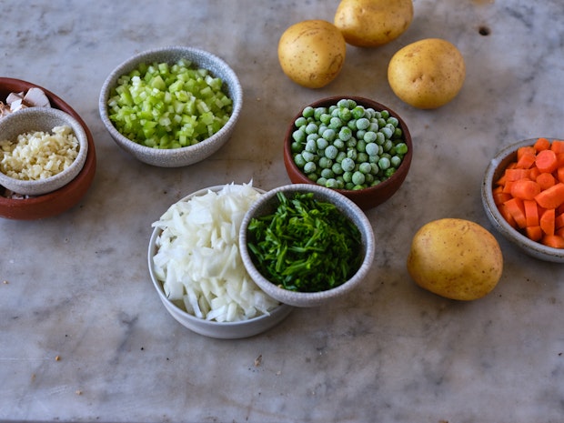 ingredients to make vegetable pot pie arrange on counter including potatoes, frozen peas, and carrots