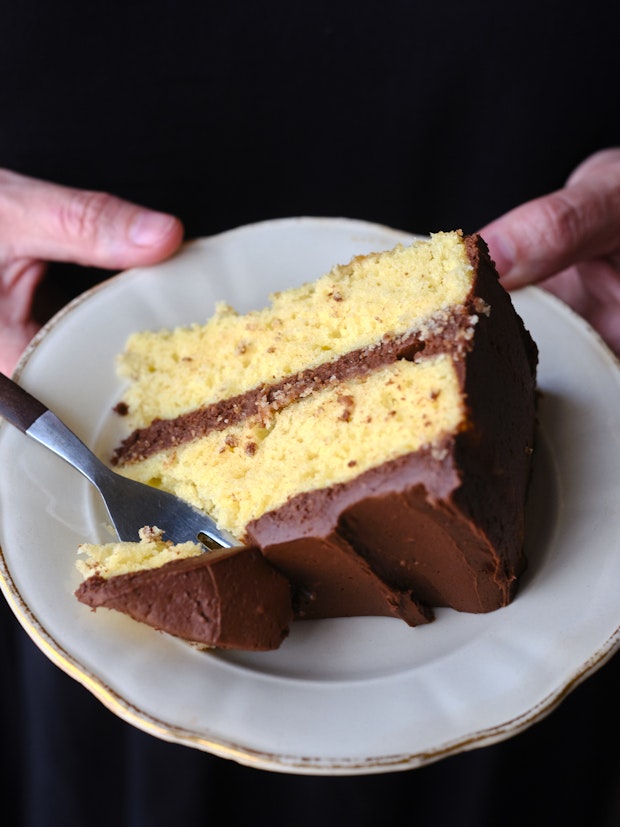 a slice of classic yellow cake with chocolate frosting being held on a plate