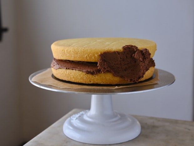 frosting a yellow cake on a cake stand with chocolate frosting