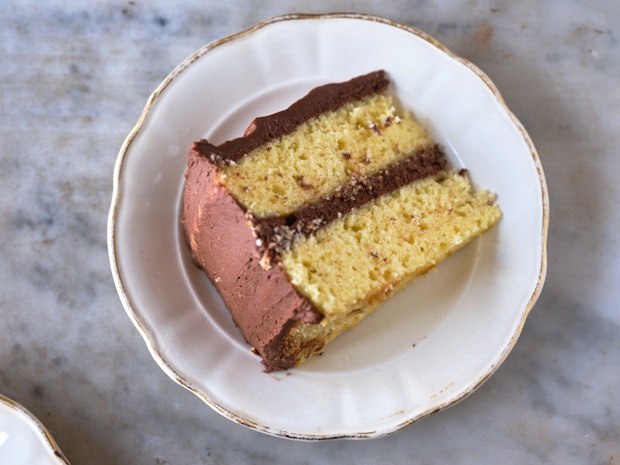 a slice of classic yellow cake with chocolate frosting being held on a plate